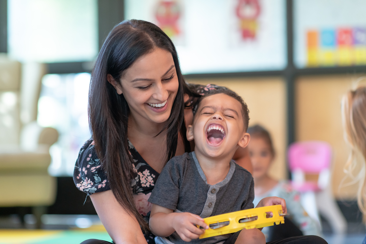 A preschool boy laughing with his teacher while playing a tambourine